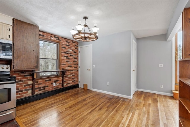 kitchen featuring light wood finished floors, baseboards, appliances with stainless steel finishes, and an inviting chandelier