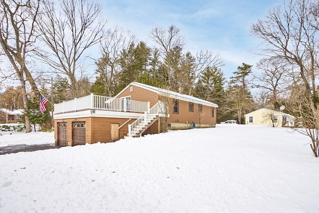 snow covered rear of property featuring a garage and stairs