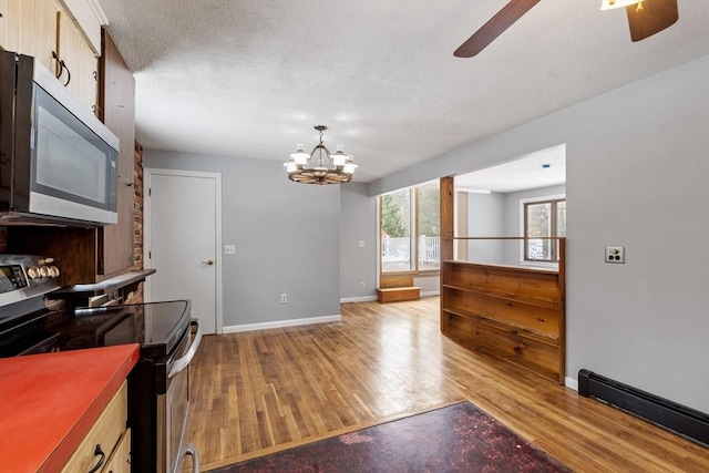 kitchen with baseboards, stainless steel appliances, light wood-style floors, a baseboard heating unit, and ceiling fan with notable chandelier