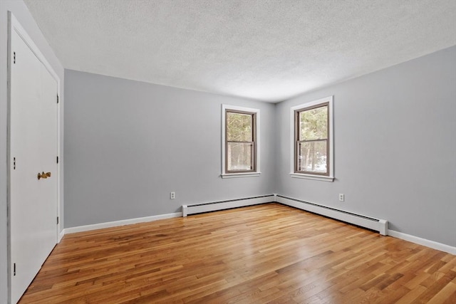 unfurnished room featuring a baseboard heating unit, a textured ceiling, baseboards, and wood finished floors