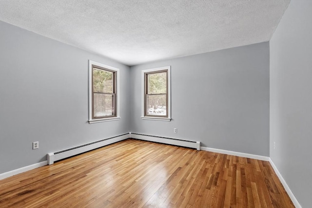 empty room with a textured ceiling, baseboard heating, wood finished floors, and baseboards