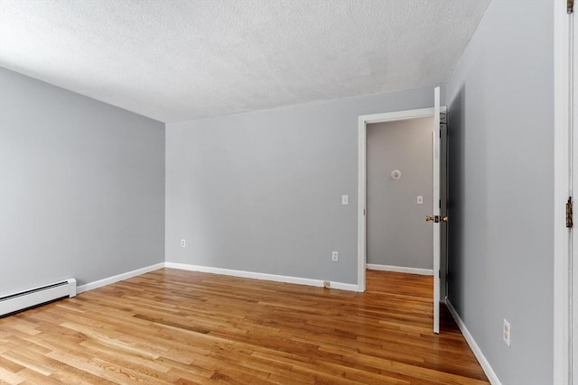 spare room featuring light wood-type flooring, a textured ceiling, baseboards, and baseboard heating