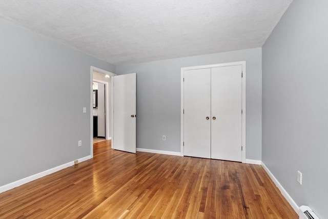 unfurnished bedroom featuring a baseboard heating unit, baseboards, and wood finished floors