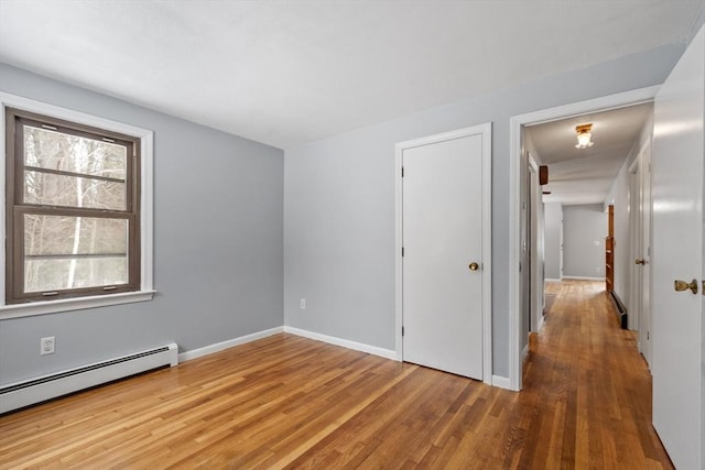 empty room featuring a baseboard heating unit, baseboards, and wood finished floors