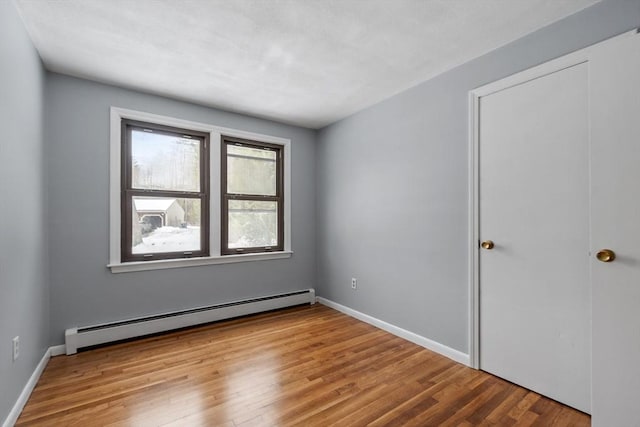 spare room featuring light wood-type flooring, a baseboard radiator, and baseboards