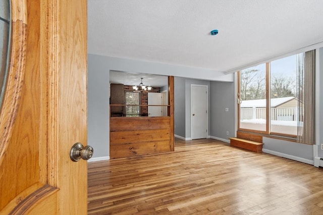 unfurnished room with baseboards, wood finished floors, and a notable chandelier