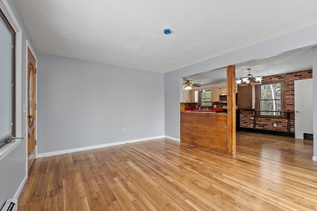 unfurnished living room with light wood-style floors, brick wall, a baseboard heating unit, and baseboards