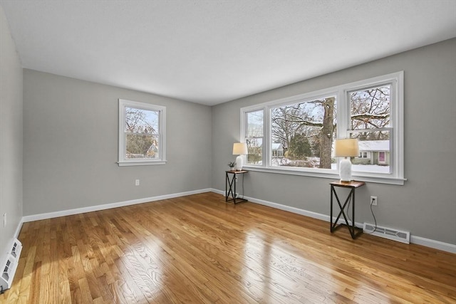 empty room featuring hardwood / wood-style floors, plenty of natural light, and a baseboard heating unit