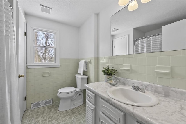 bathroom featuring vanity, toilet, a textured ceiling, and tile walls