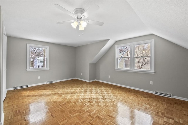 additional living space featuring light parquet flooring, lofted ceiling, a healthy amount of sunlight, and a textured ceiling