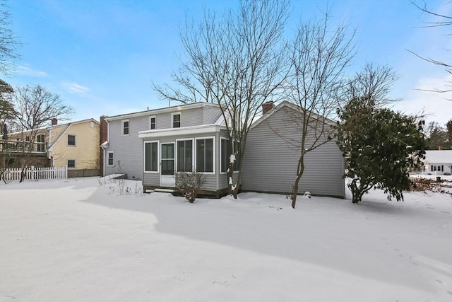 snow covered rear of property with a sunroom