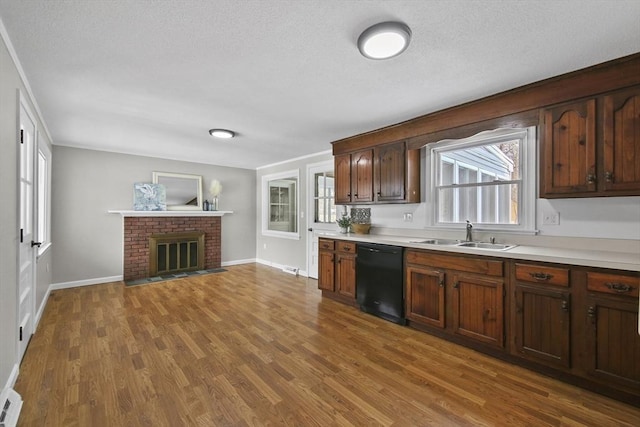 kitchen with sink, a brick fireplace, a textured ceiling, dishwasher, and hardwood / wood-style flooring