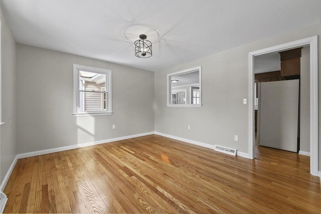 unfurnished bedroom featuring wood-type flooring, fridge, and a chandelier