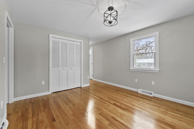 unfurnished bedroom featuring an inviting chandelier, light wood-type flooring, and a closet