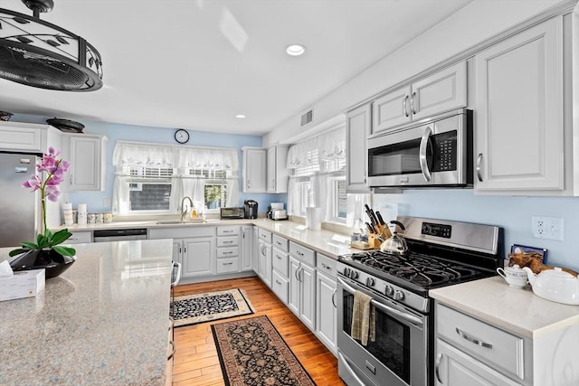 kitchen featuring light stone countertops, stainless steel appliances, sink, hanging light fixtures, and light hardwood / wood-style flooring