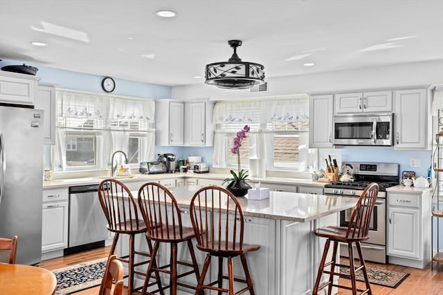 kitchen with white cabinets, a kitchen island, decorative light fixtures, stainless steel appliances, and light hardwood / wood-style floors