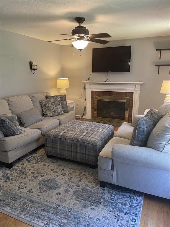 living area featuring a glass covered fireplace, ceiling fan, and wood-type flooring