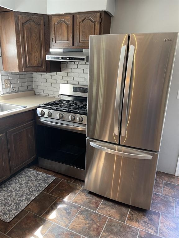 kitchen featuring stone tile flooring, decorative backsplash, light countertops, ventilation hood, and stainless steel appliances