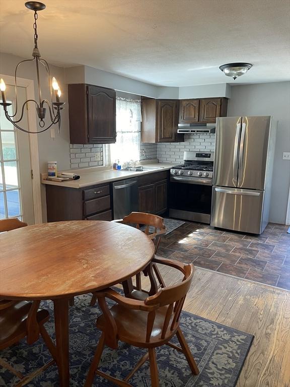 kitchen with dark brown cabinetry, light countertops, stainless steel appliances, backsplash, and under cabinet range hood
