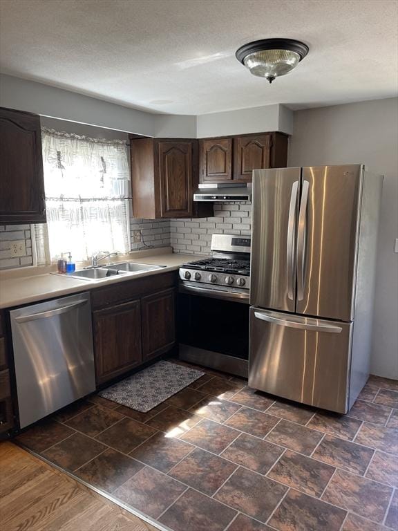 kitchen with appliances with stainless steel finishes, dark brown cabinets, a sink, light countertops, and under cabinet range hood
