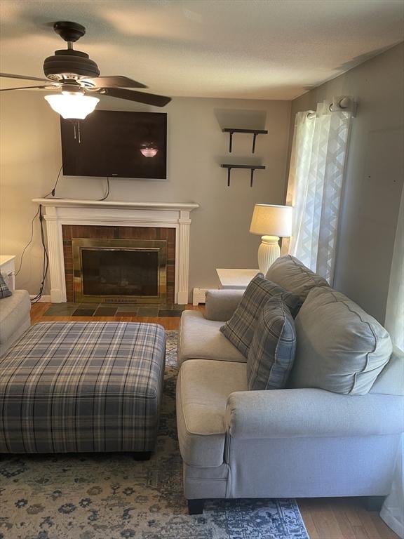 living area featuring a ceiling fan, a tiled fireplace, and wood finished floors