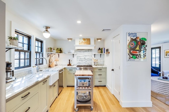 kitchen featuring a wealth of natural light, wood counters, sink, stainless steel dishwasher, and light hardwood / wood-style flooring