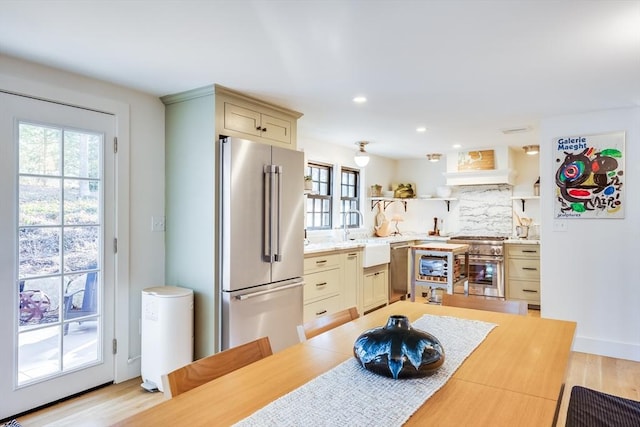 kitchen featuring high end appliances, decorative backsplash, sink, premium range hood, and light hardwood / wood-style flooring