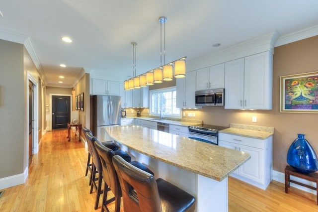 kitchen featuring appliances with stainless steel finishes, a breakfast bar area, ornamental molding, light stone countertops, and light wood-style floors