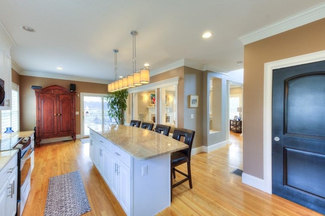 kitchen with electric range, white cabinets, light wood-type flooring, a center island, and a kitchen bar