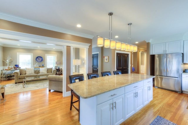 kitchen with light wood-type flooring, freestanding refrigerator, white cabinetry, and a breakfast bar area