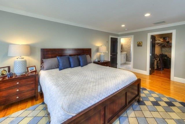 bedroom with light wood finished floors, visible vents, ornamental molding, a walk in closet, and a closet