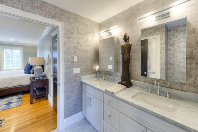 ensuite bathroom with ornamental molding, a sink, baseboards, and wood finished floors