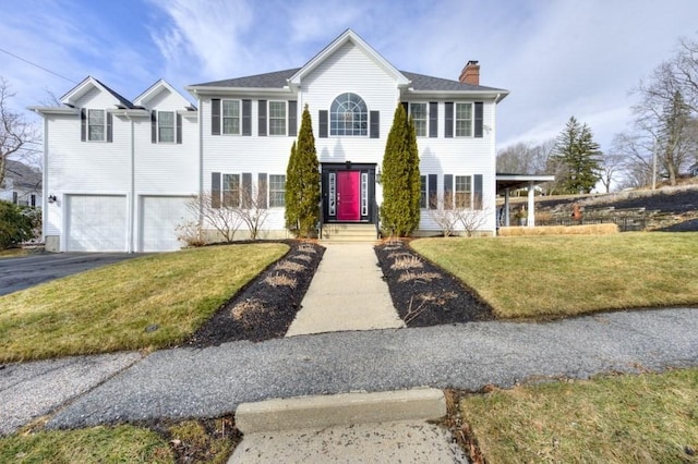 colonial home featuring a front yard, a garage, driveway, and a chimney