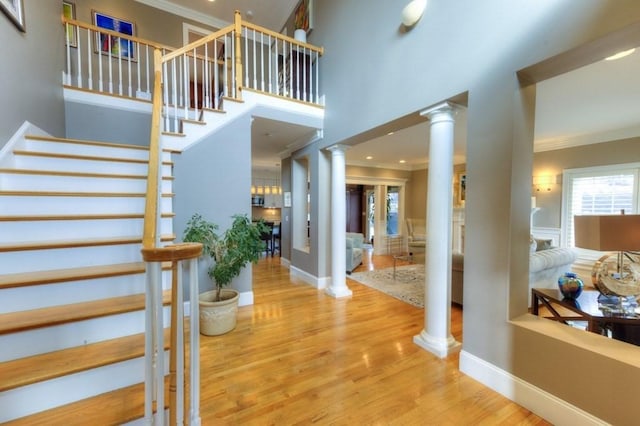 foyer featuring crown molding, baseboards, wood finished floors, and ornate columns