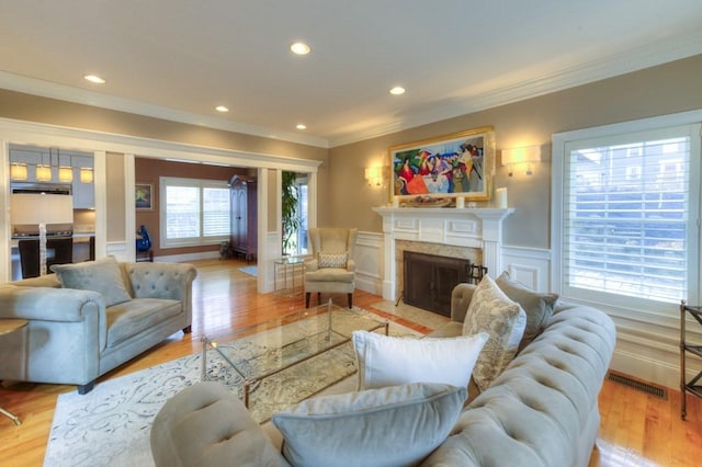 living room featuring ornamental molding, a high end fireplace, visible vents, and light wood finished floors