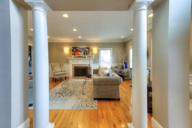 living area with ornamental molding, a high end fireplace, ornate columns, and wood finished floors