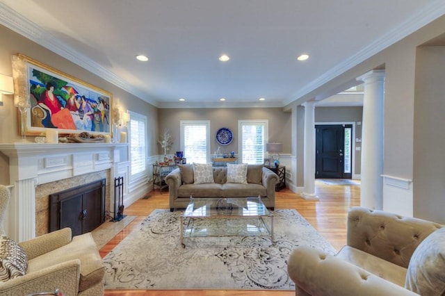 living area featuring light wood-style floors, a fireplace, ornate columns, and ornamental molding