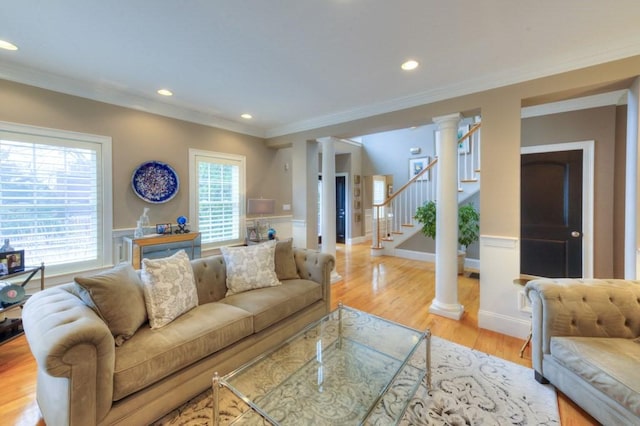 living room featuring a wainscoted wall, crown molding, stairway, light wood-style floors, and ornate columns