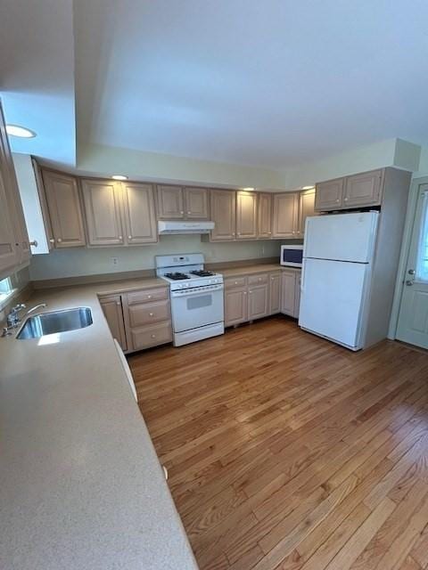 kitchen with under cabinet range hood, light countertops, light wood-style flooring, white appliances, and a sink