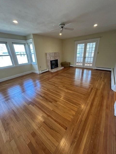 unfurnished living room with a baseboard heating unit, a healthy amount of sunlight, wood finished floors, and a fireplace