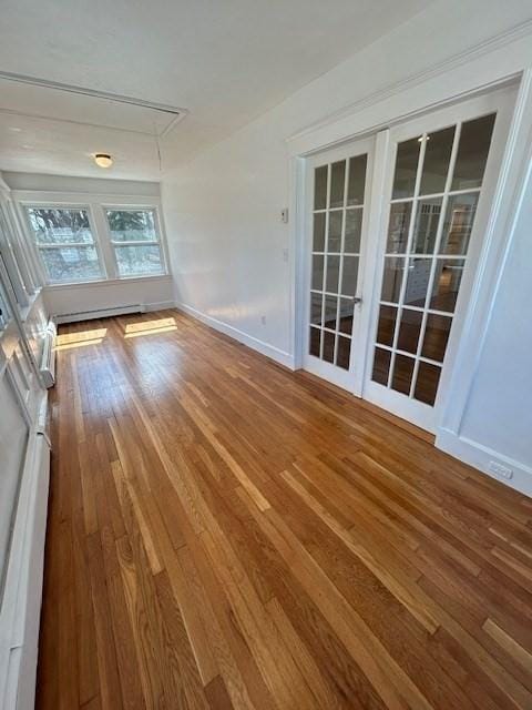 interior space featuring a baseboard radiator, attic access, baseboards, and wood-type flooring