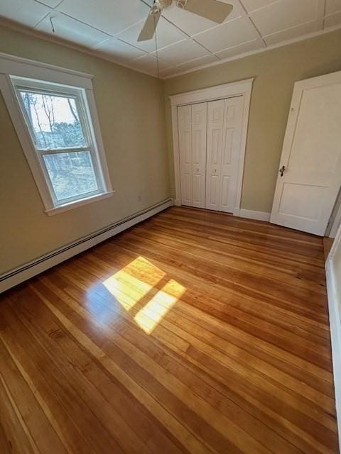 unfurnished bedroom with a baseboard heating unit, baseboards, a closet, and light wood finished floors