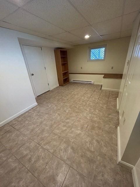 below grade area featuring a drop ceiling, a baseboard heating unit, and baseboards