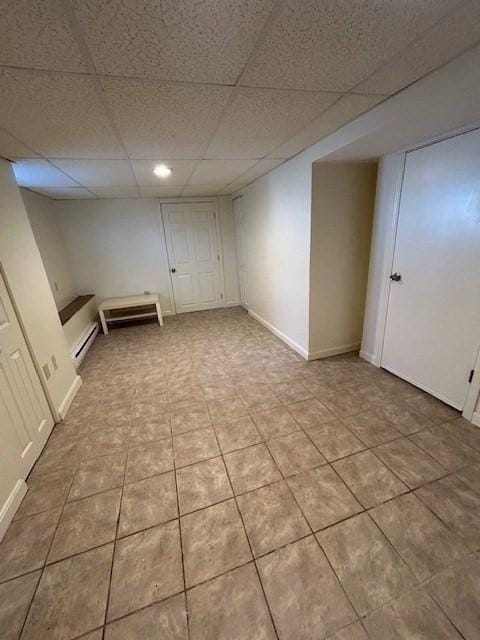 finished below grade area with a paneled ceiling, a baseboard radiator, baseboards, and light tile patterned flooring