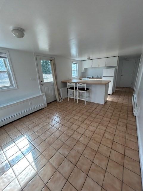 kitchen with freestanding refrigerator, a peninsula, a breakfast bar area, white cabinets, and light countertops