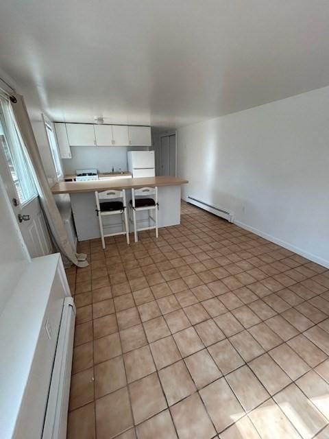 kitchen featuring light countertops, a peninsula, freestanding refrigerator, white cabinetry, and a baseboard radiator