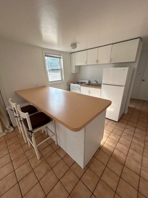 kitchen with light countertops, light tile patterned floors, a peninsula, white appliances, and white cabinetry