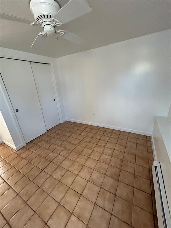 unfurnished bedroom featuring a closet, baseboards, a baseboard heating unit, and ceiling fan