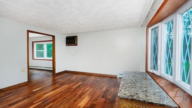 spare room featuring a wall unit AC, a baseboard radiator, hardwood / wood-style flooring, and a wealth of natural light