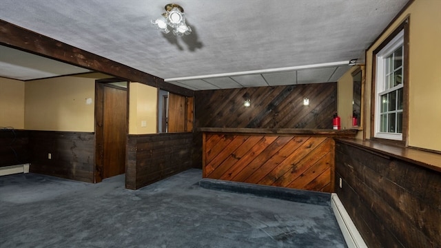 interior space with a baseboard radiator, dark carpet, wooden walls, and a textured ceiling